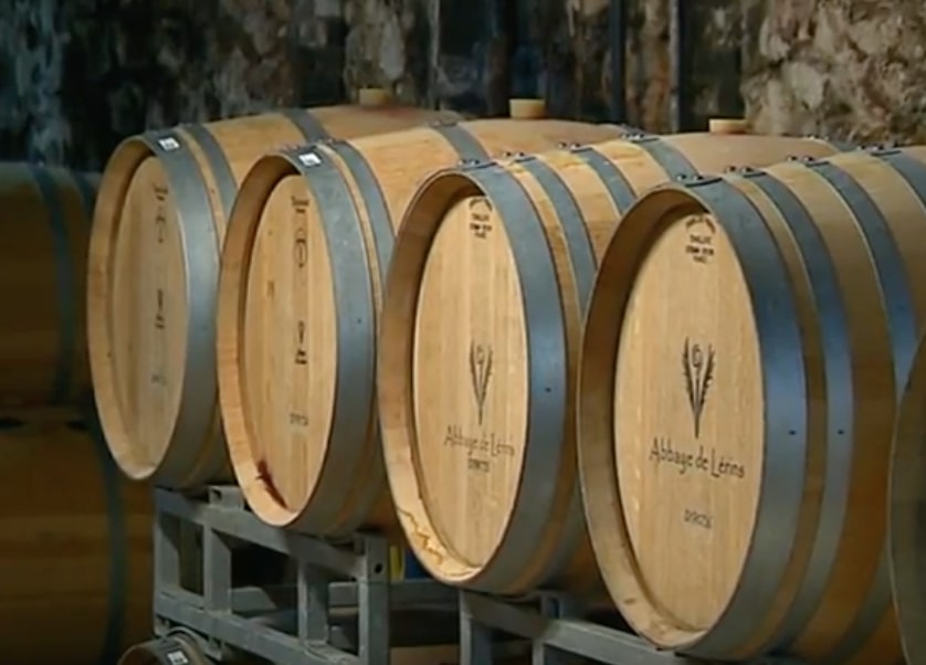 Rangée de barriques en chêne marquées Abbaye de Lérins dans le chai de vieillissement voûté en pierre